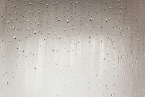 Water droplets of various sizes clinging to a smooth, light-coloured surface, with some streaks visible