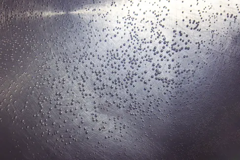 Macro shot of small water droplets on a textured metal surface, creating a unique pattern.